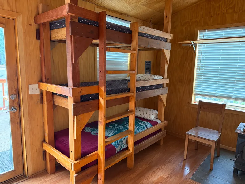 A room with a hand-built triple bunk, a window and a door to the deck