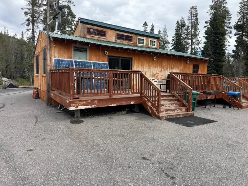 The cabin from outside: a wooden cabin with a green roof, a deck with railings and grills, solar panels