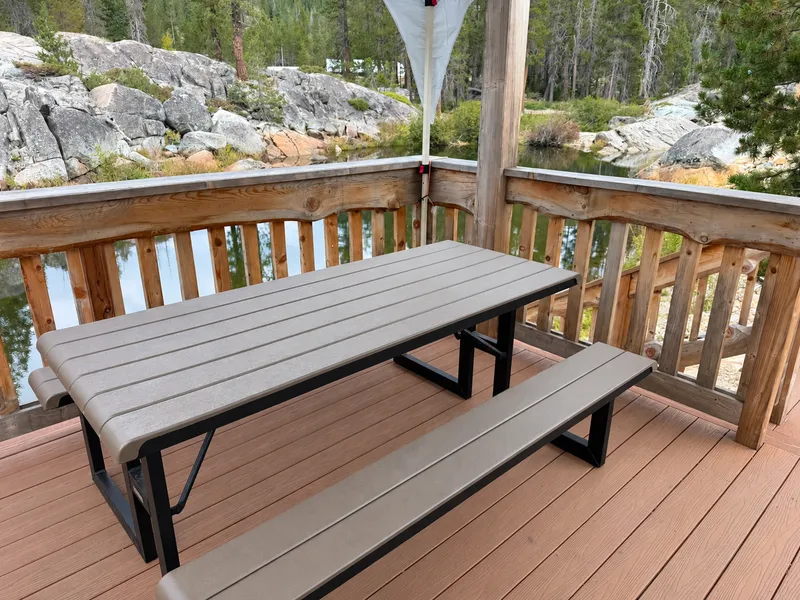 The deck by the sauna above the river pool: a table with benches, carved railings, granite boulders and pines beyond