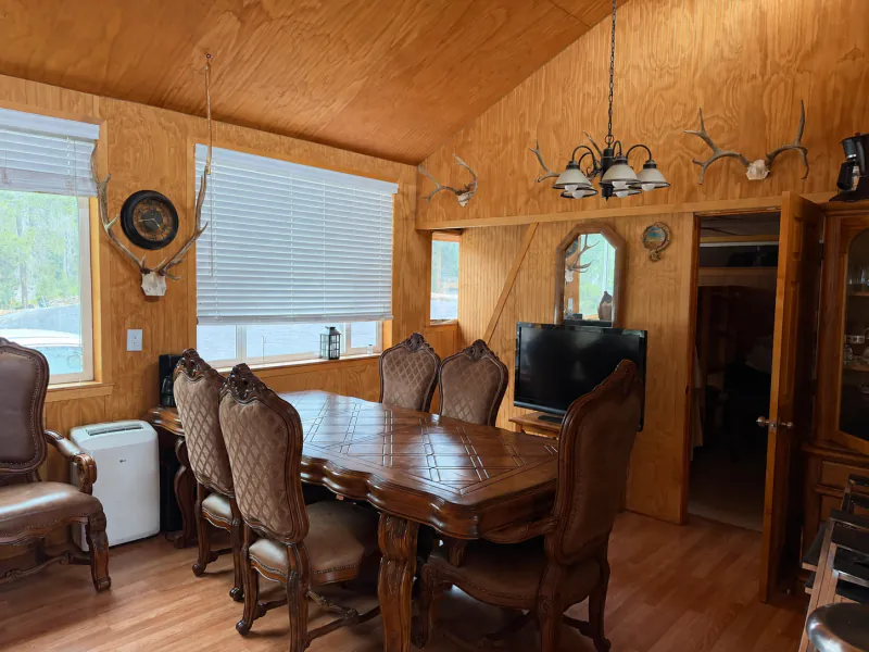 Cabin dining room with a carved wooden table, a chandelier and a window to the forest