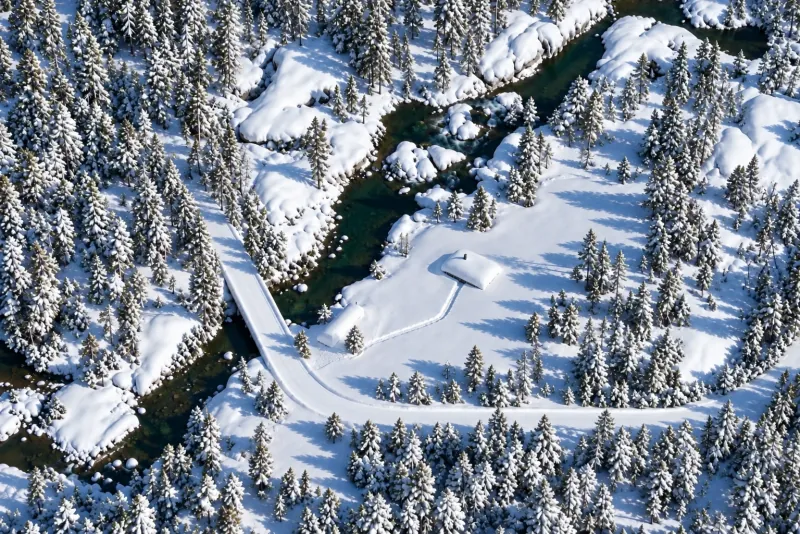 The same view in winter: the clearing, the road and the bridge under deep snow, the cabin and the sauna buried to the roof, a trench dug to the cabin door