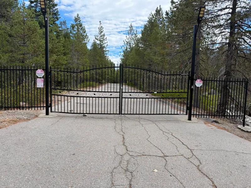 The property gate: iron gates across a paved road, pine forest behind