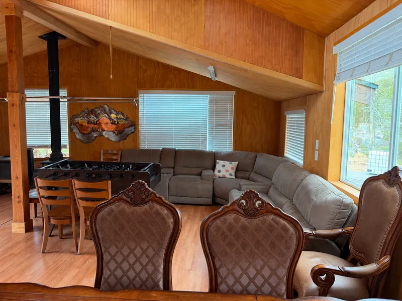 Living room: a big sectional sofa, a foosball table, the wood-stove pipe and windows to the forest