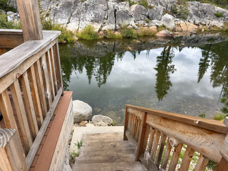 Wooden steps go down from the deck into a quiet pool between granite boulders
