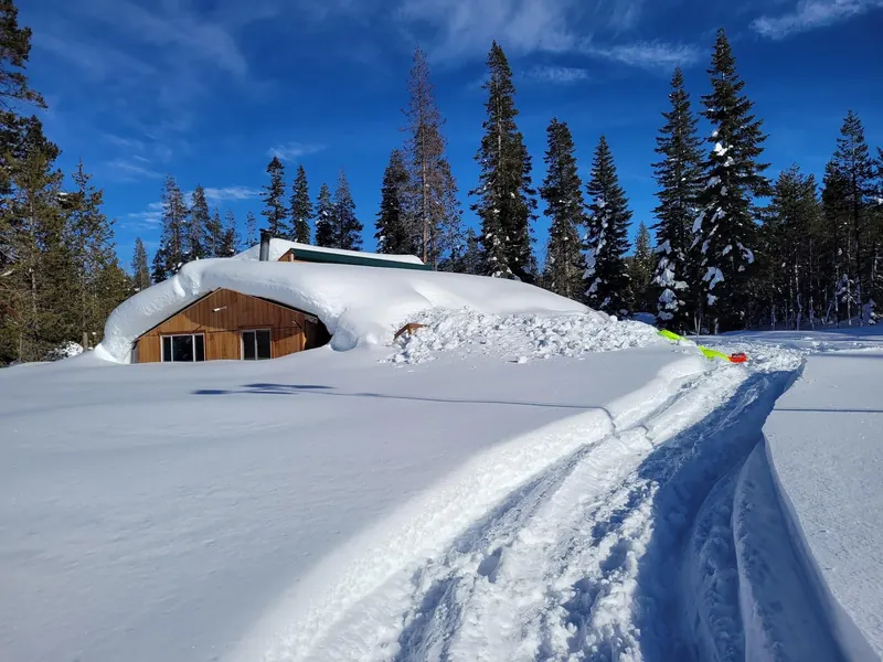 The green-roofed cabin almost buried in snow, with a snowmobile track leading to it